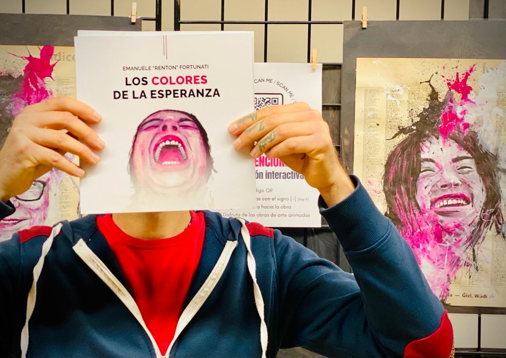 The artist holding the book Los colores de la esperanza in front of his face, at the exhibition